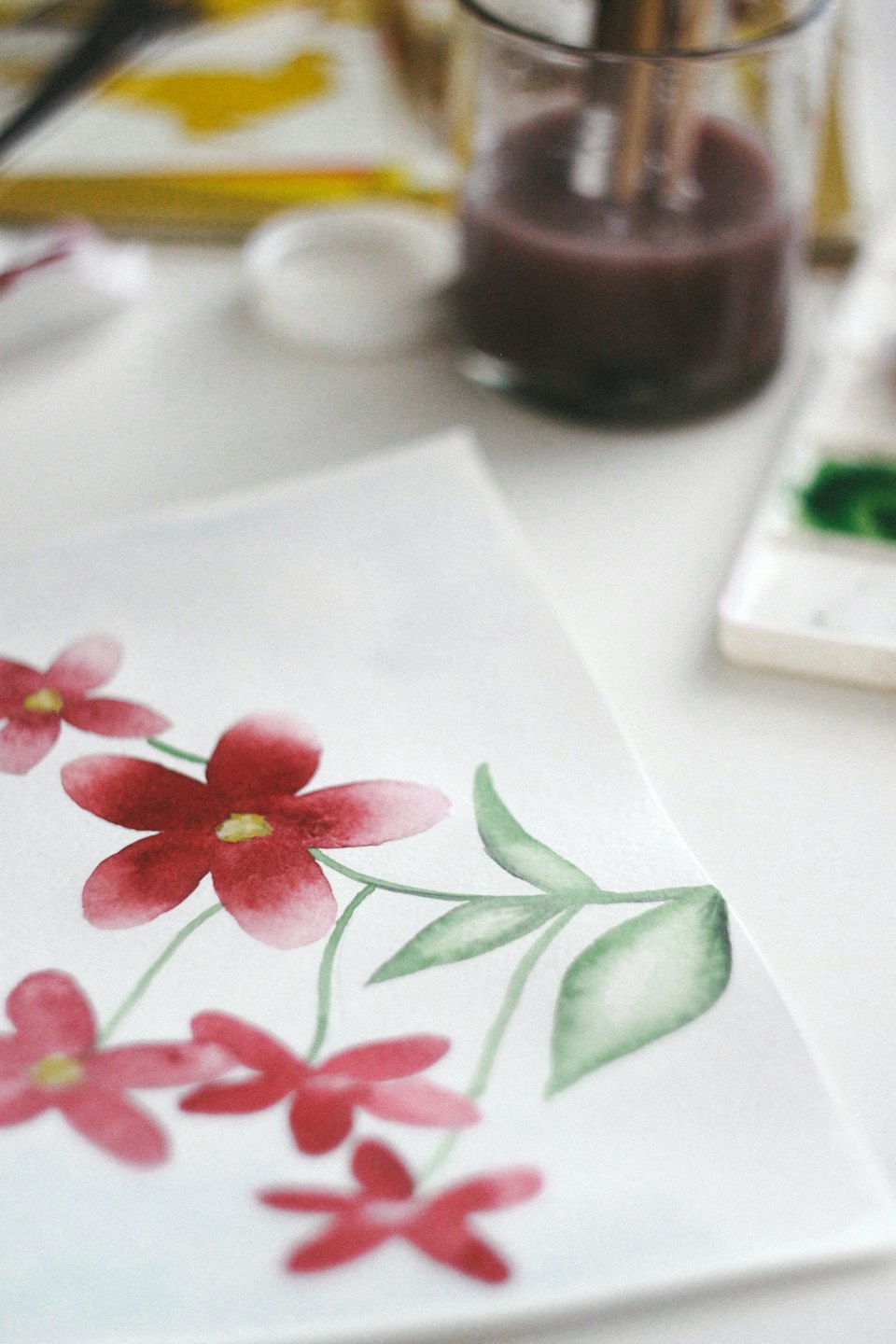 Pintura de acuarela de flores rojas y hojas verdes sobre papel.