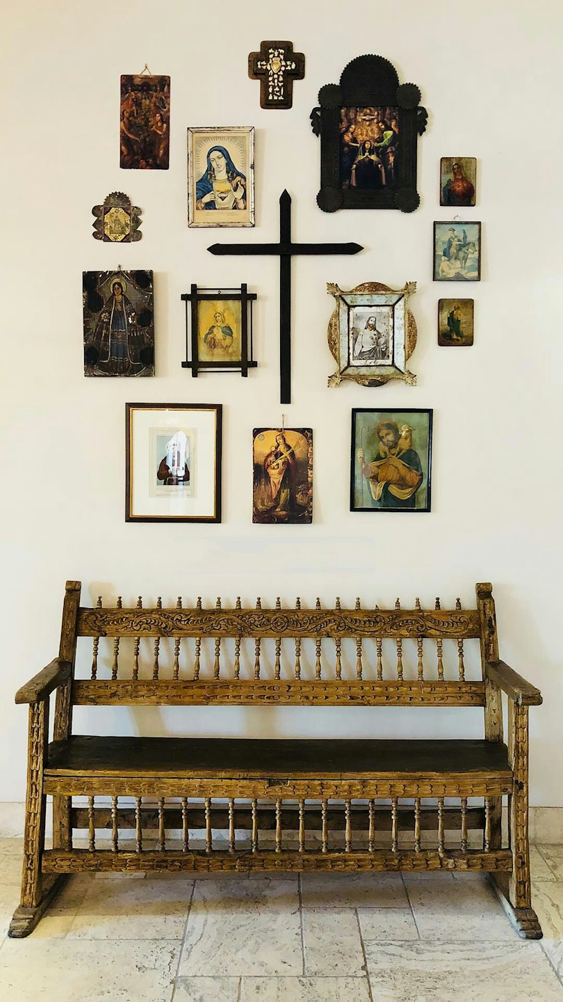 Pinturas religiosas y cruces cuelgan sobre un banco antiguo de madera.