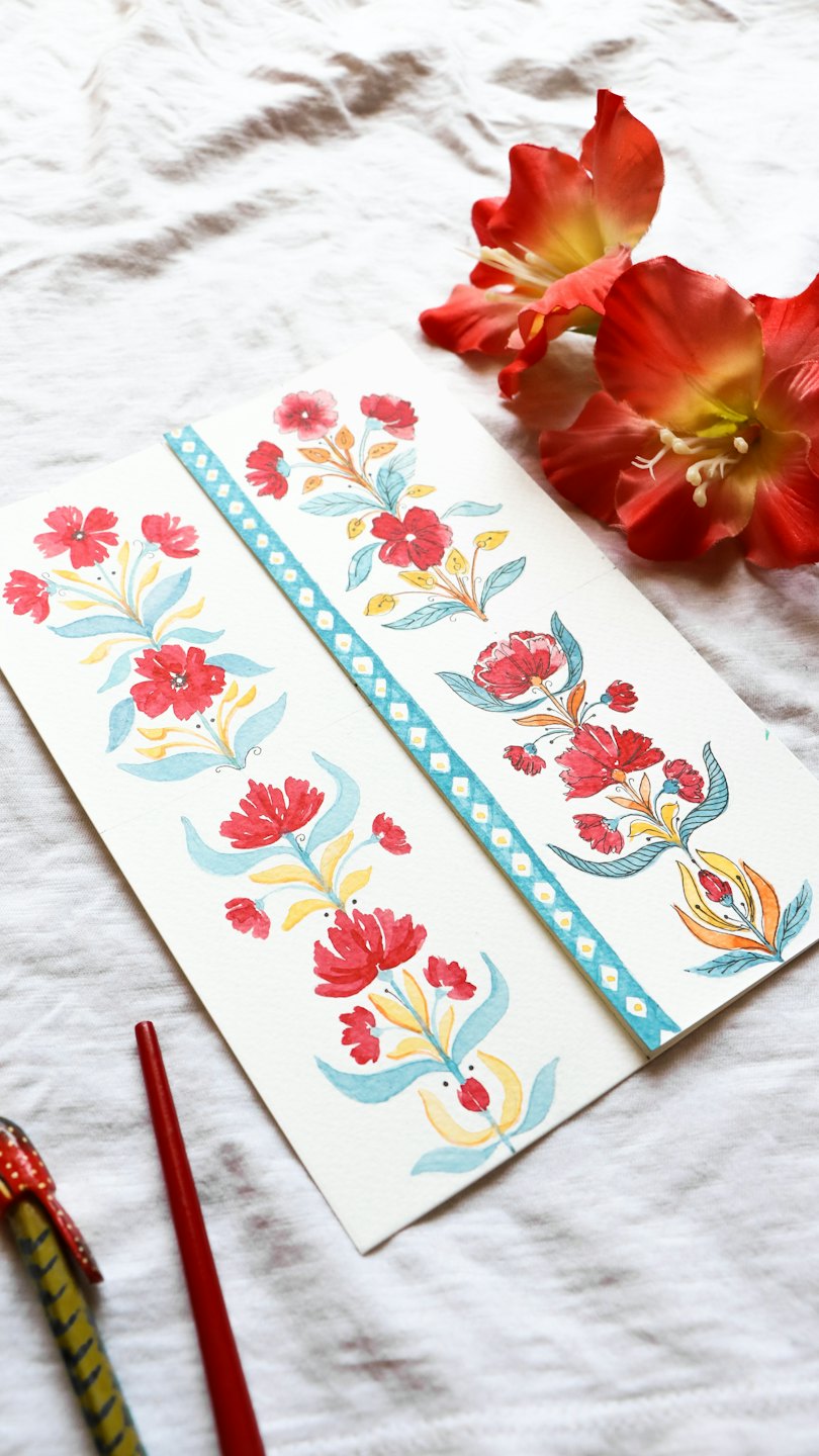 Hojas de papel pintadas a mano con flores, pinceles y tela.