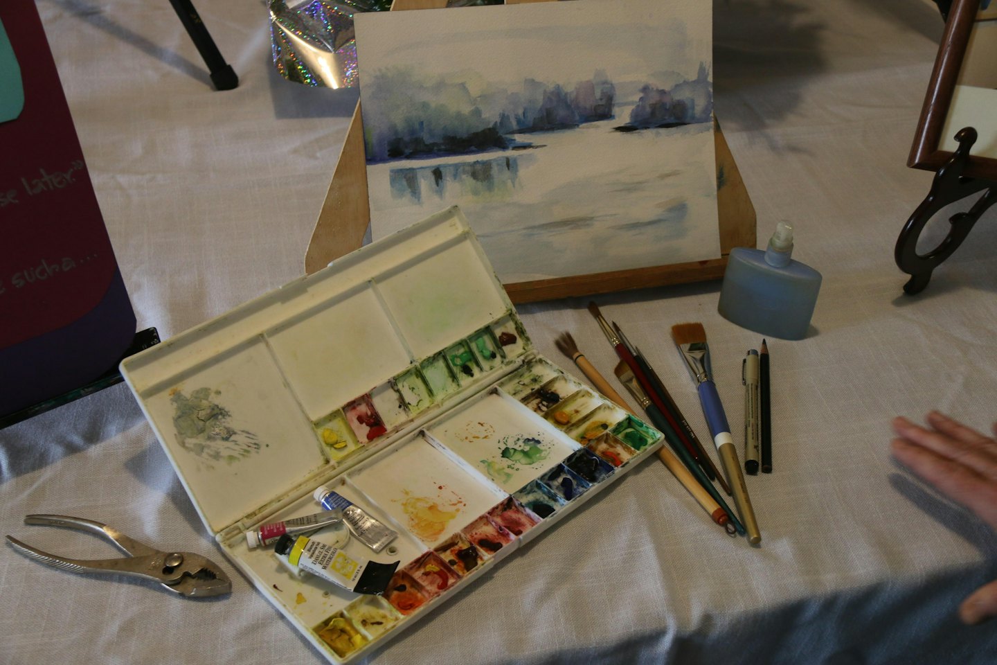 Espacio de trabajo de artista con acuarelas y pinceles sobre un mantel.