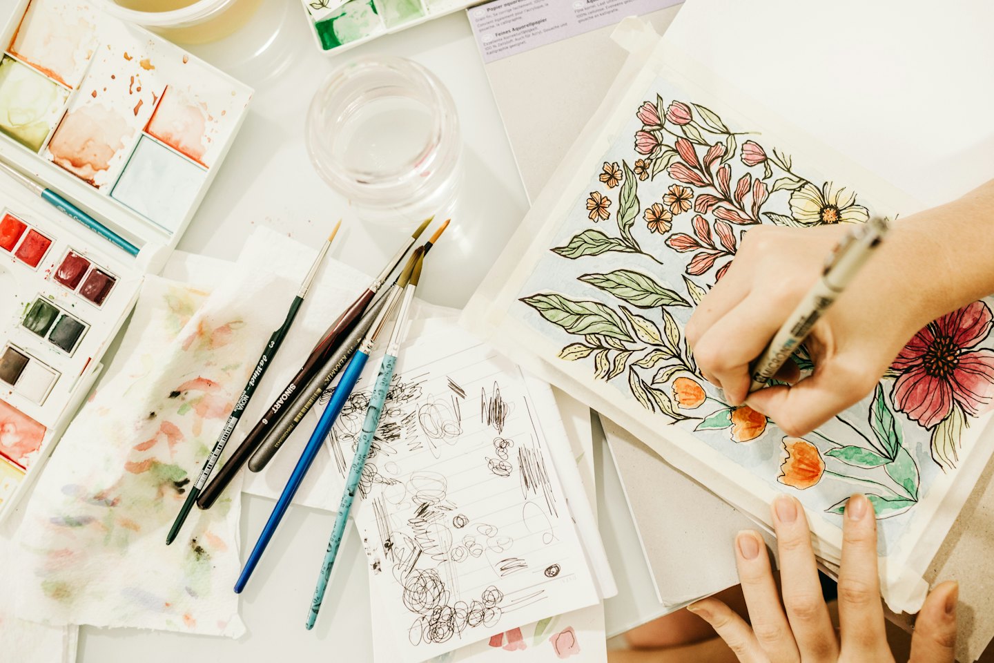 Manos pintando un delicado patrón floral con acuarelas y pluma.
